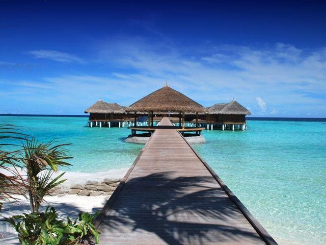 A photo of a hut out on a bright blue sea in a holiday destination